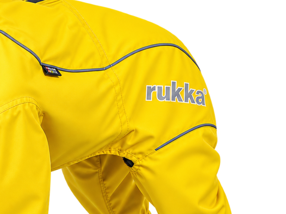 Lähikuva keltaisesta Rukka Pets Protect -sadehaalarista, jossa näkyvät kangas, heijastavat tereet ja Rukka-logo.